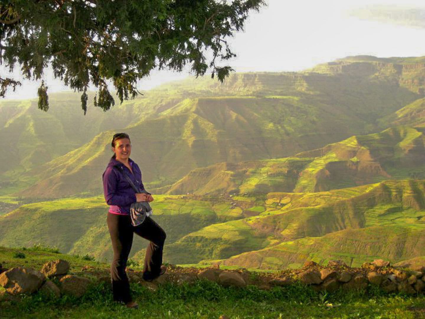 Woman on a mountain in Ethiopia surrounded by lush landscape.