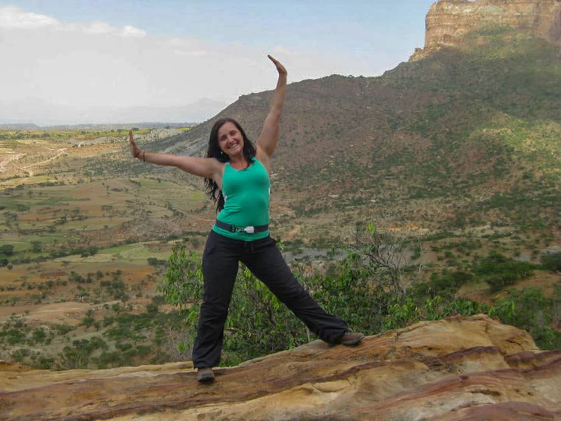 Woman on a rock in Ethiopia against a backdrop of lush landscape.
