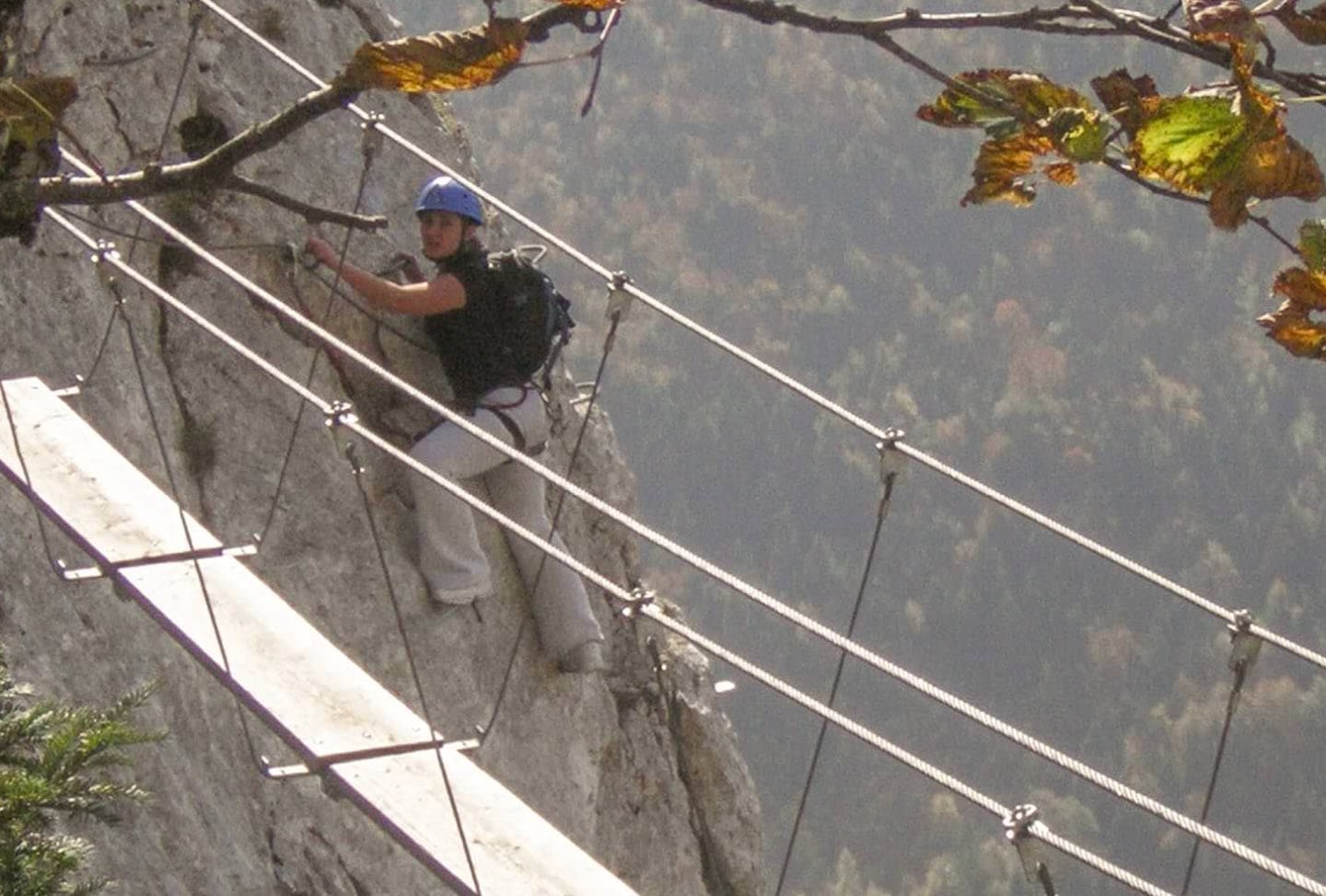 Girl rock climbing via ferrata style, attached to a steel cable by equipment.