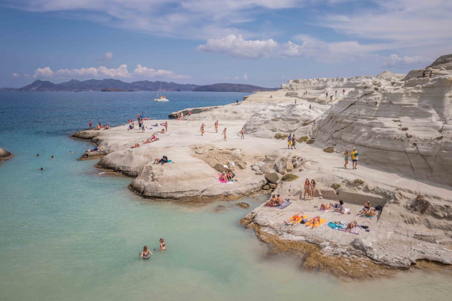 drone shot of people hanging out on the rocks of a Milos beach