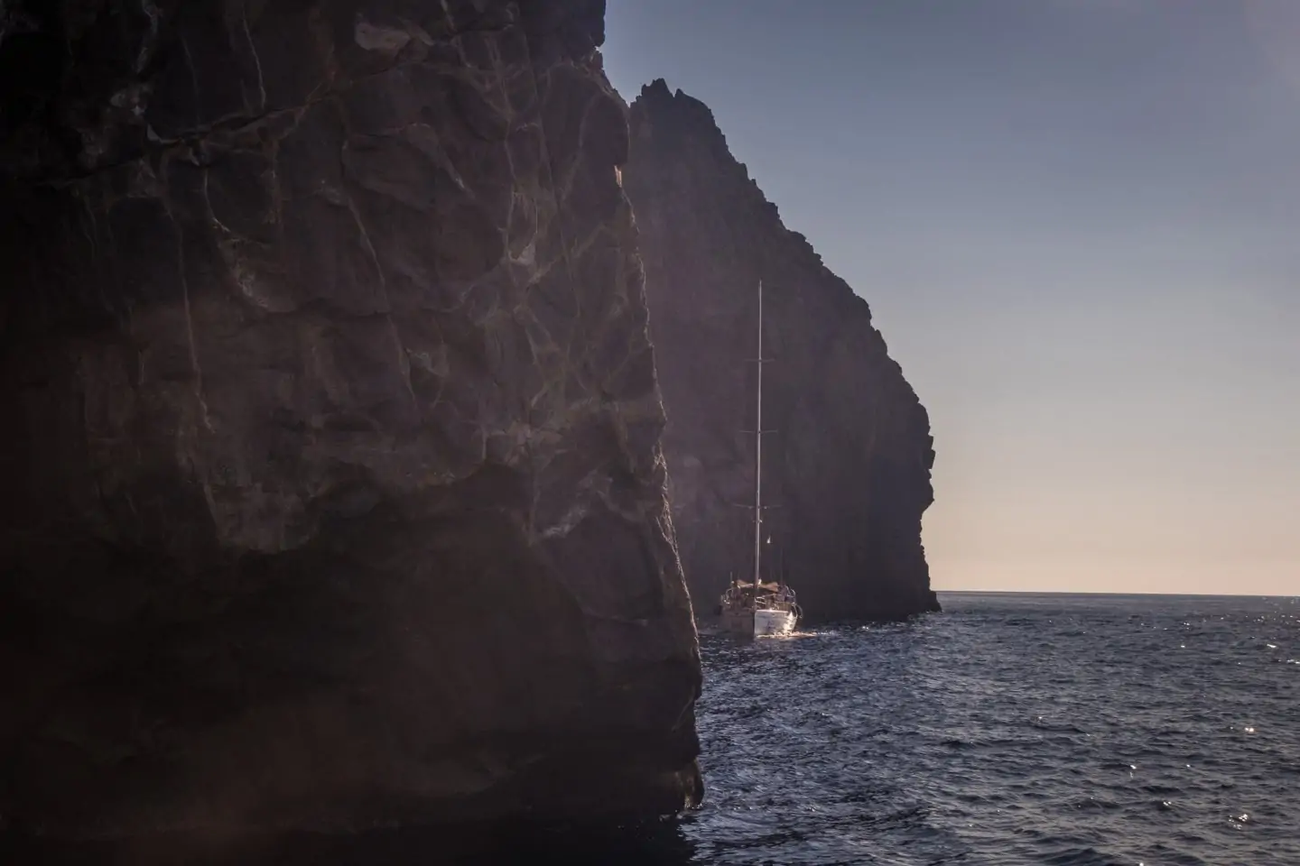 a sailing boat near jagged rocks coming out of the water near Cape Vani in Milos