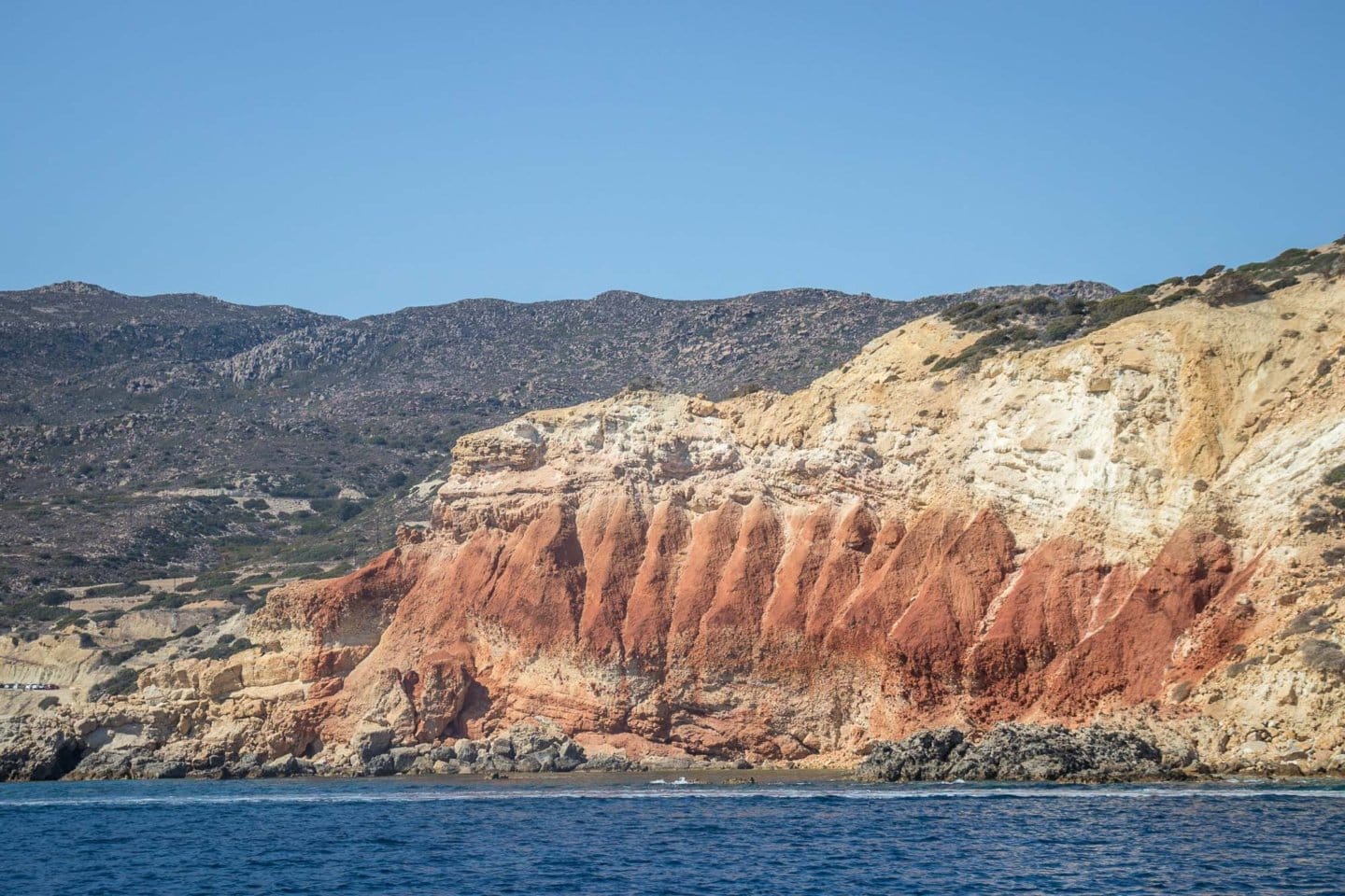 jagged red volcanic rock near a Milos beach along the Aegean Sea