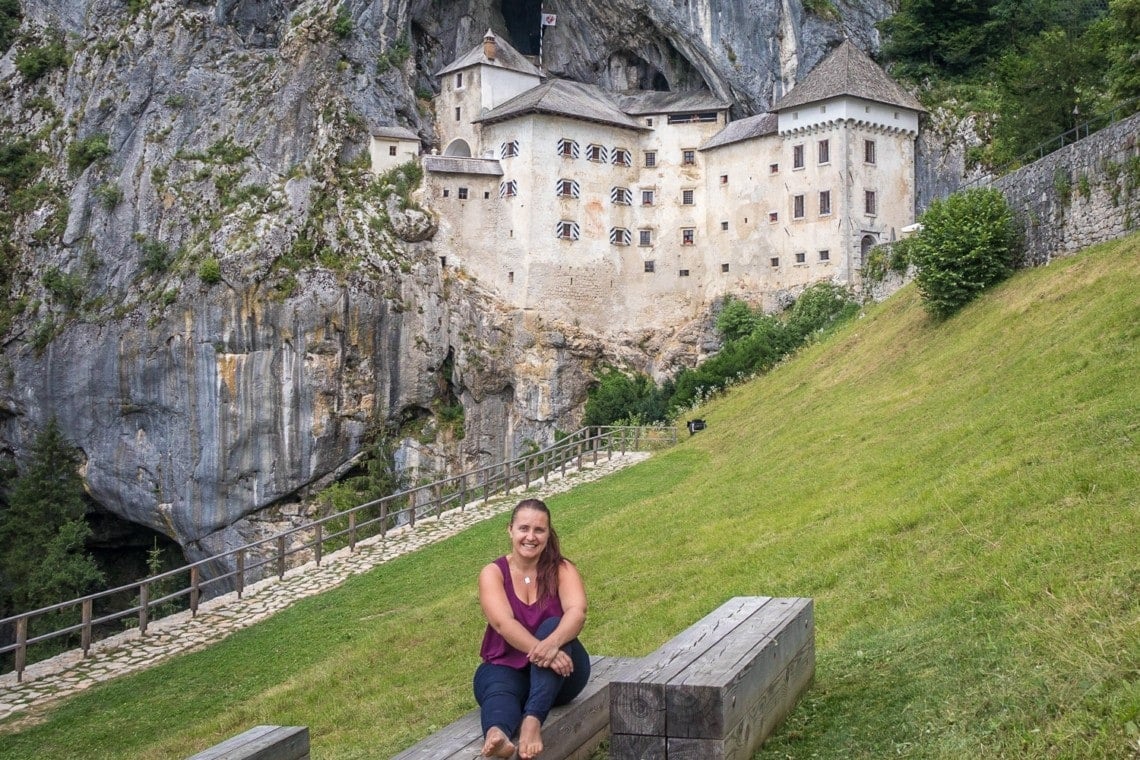 girl sitting on a bench in front of Predjama castle in Slovenia