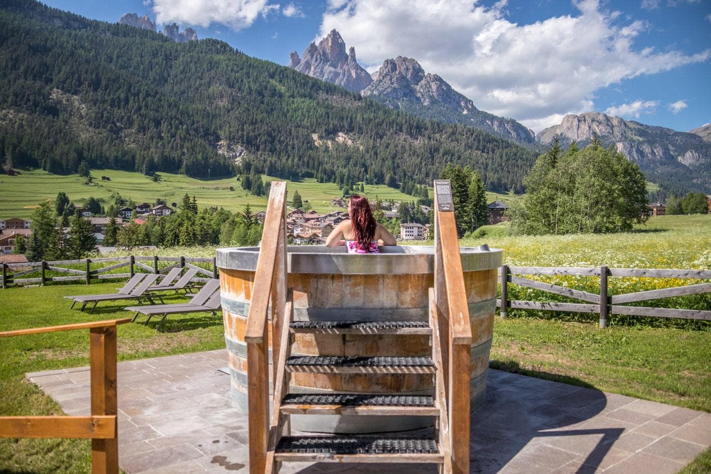 woman in a round hot tub in an open area surrounded by the Dolomite mountains