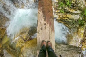 woman on a wooden ledge crossing a waterfall in trentino