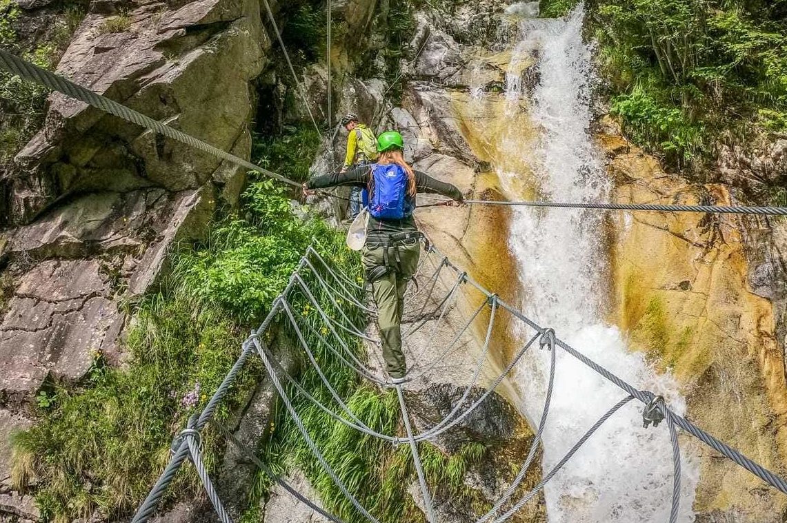 woman crossing a steel rope bridge on a via ferrata route in valle del vanoi