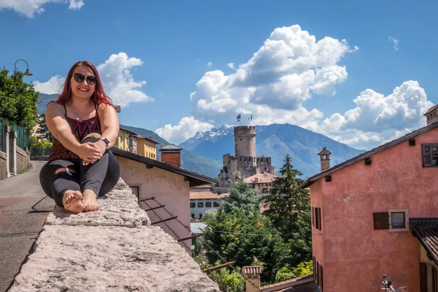 woman on a ledge with a view of trento castle from a viewpoint